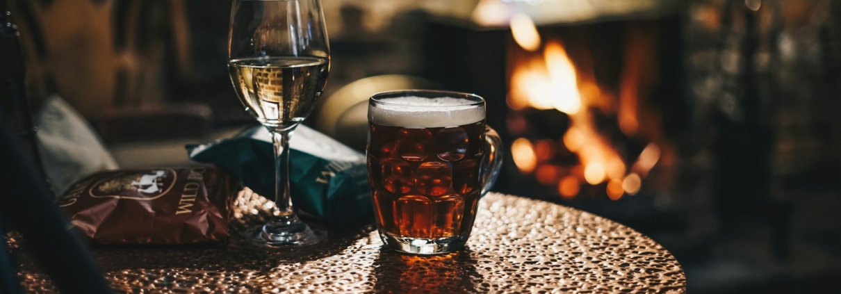 Ein Glas dunkles Bier auf einem Kupfertisch vor einem brennenden Kamin