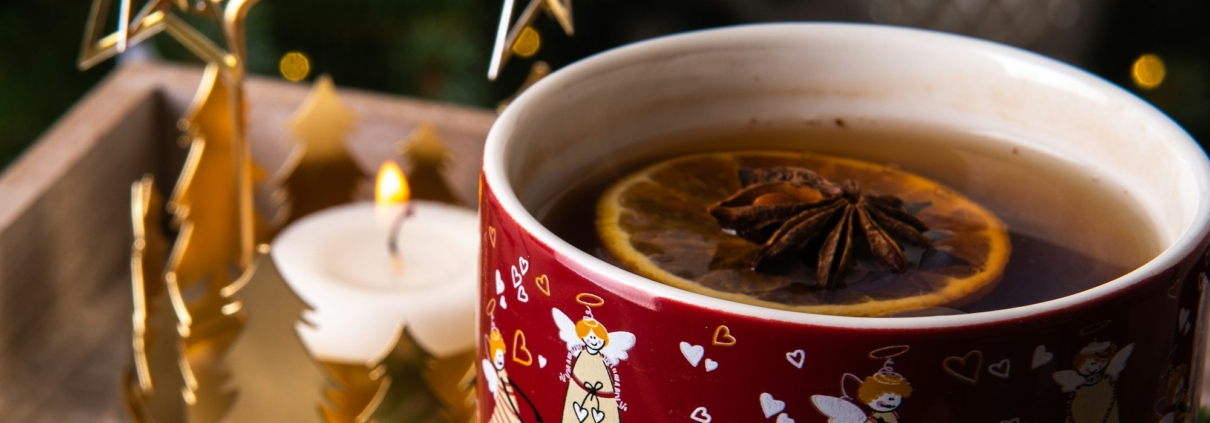 Rote Tasse mit Tee, Orangenscheibe und Sternanis neben einer Weihnachtspyramide